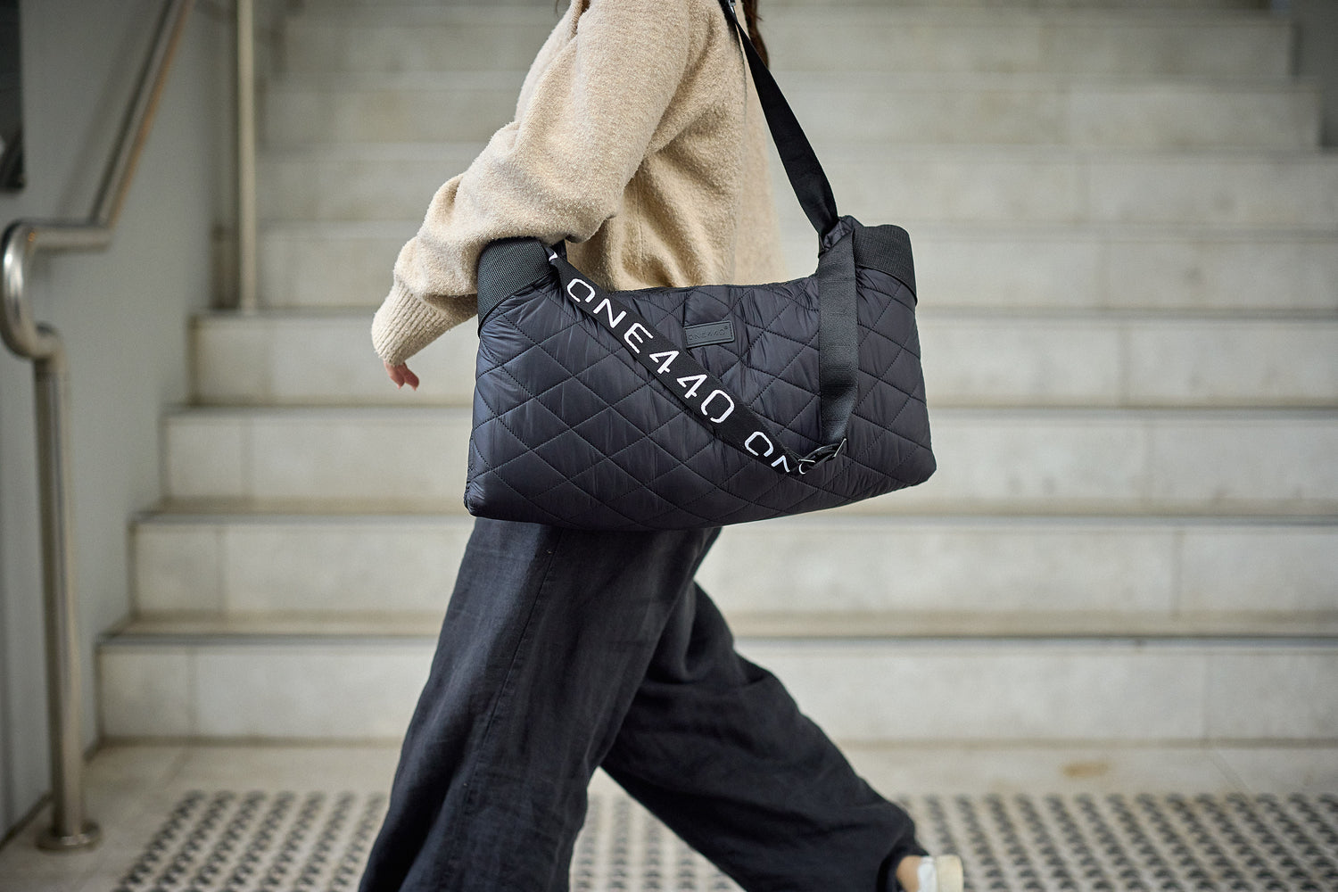 Person walking with a black quilted one440 bag on a staircase