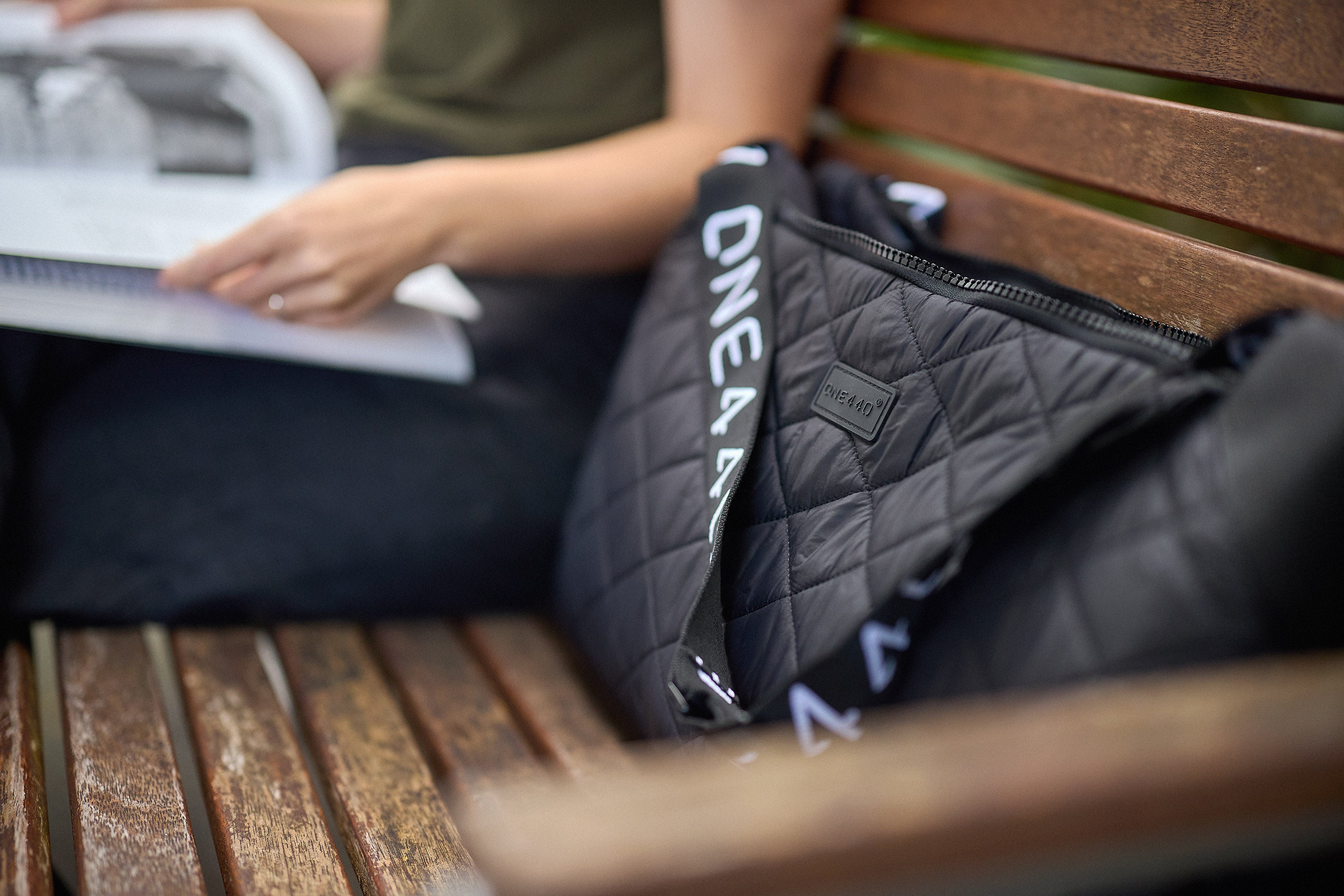 Person sitting on a wooden bench with a black quilted bag featuring 'one440' branding.