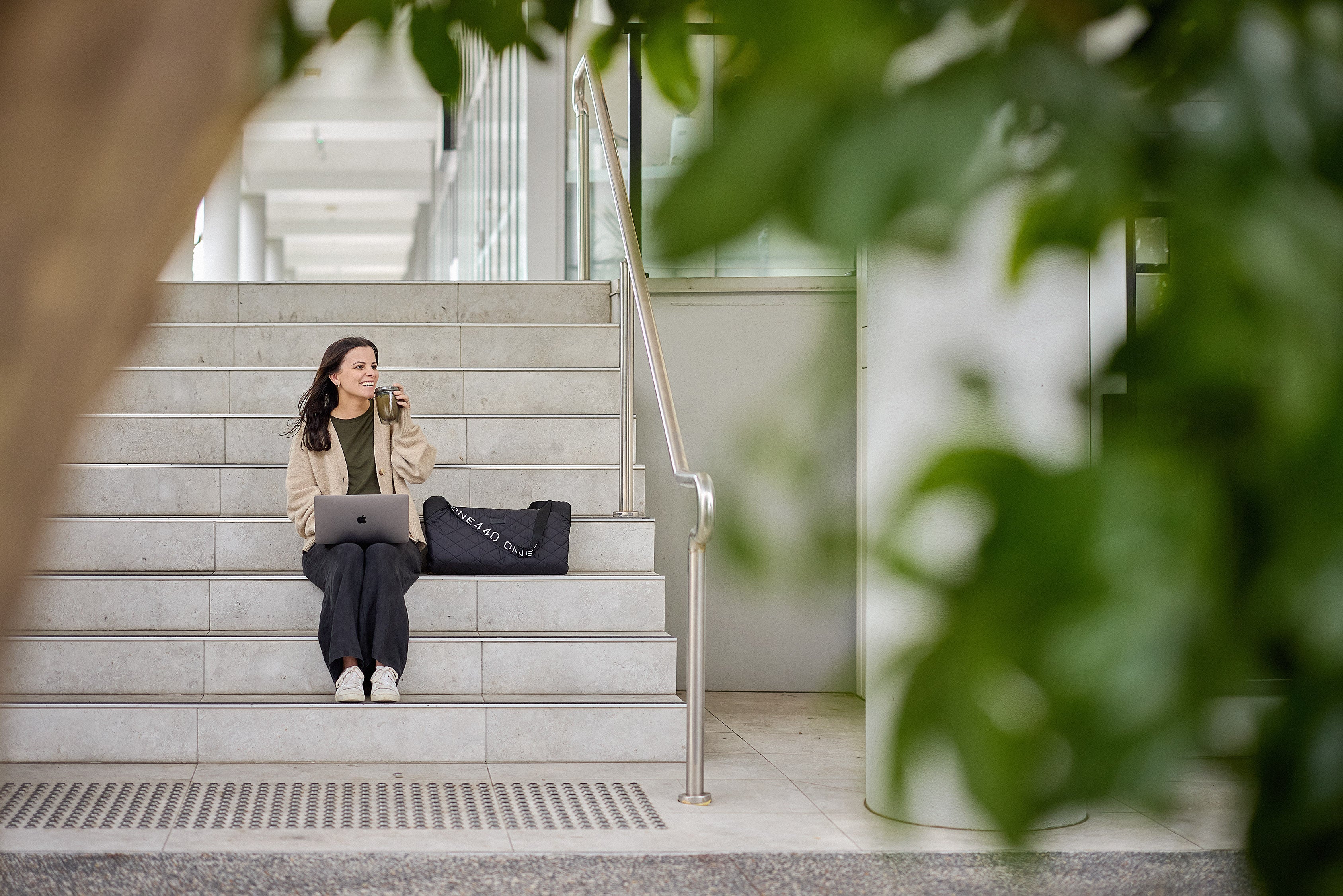 Woman sitting on steps with a one440 laptop and bag, surrounded by greenery