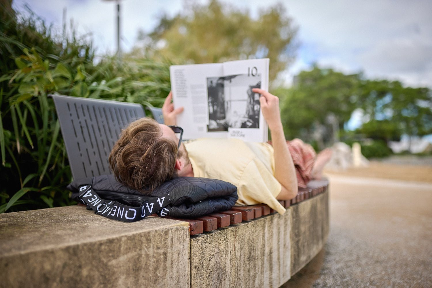 Person lying on a one440 pillow on a bench reading a magazine with a scenic background
