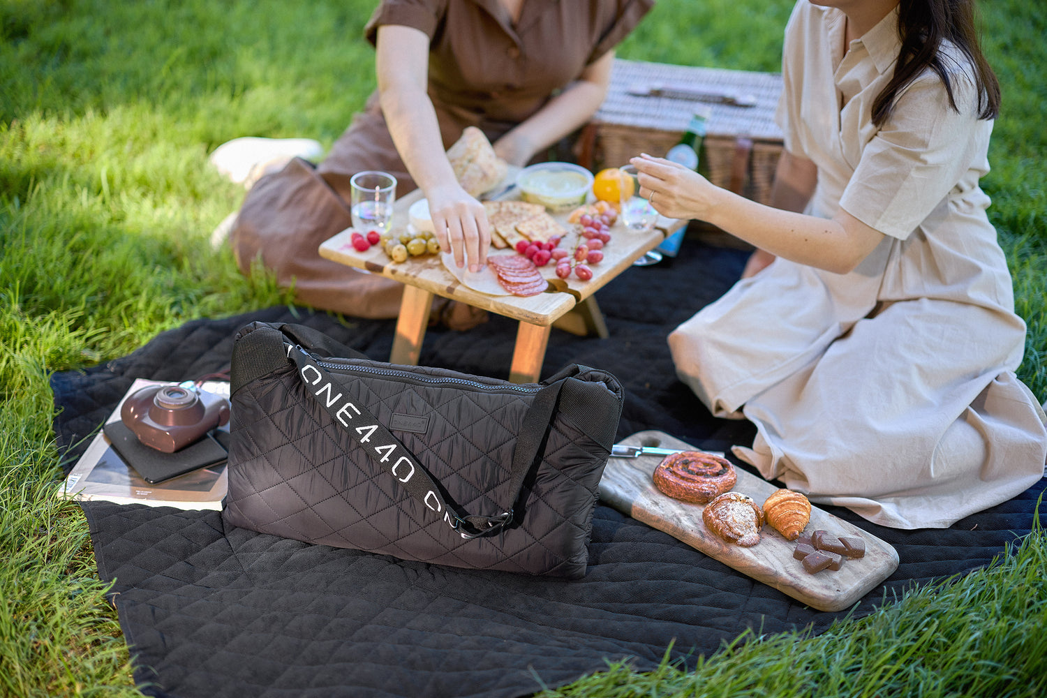 Two people having a picnic with a one440 bag on a grassy area.