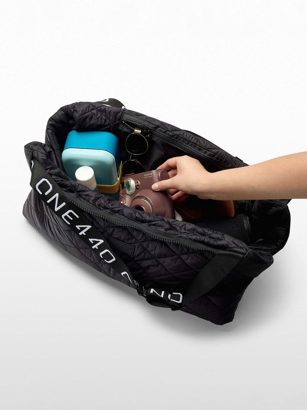 Black one440 bag with 'ONE440' branding, containing a camera and other items on a white background.