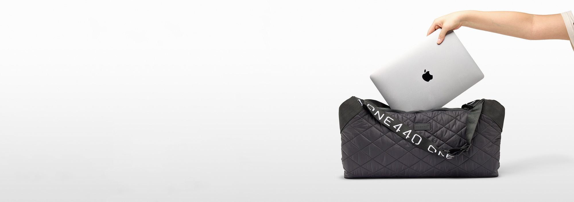 Person placing a silver laptop into a one440 backpack on a white background
