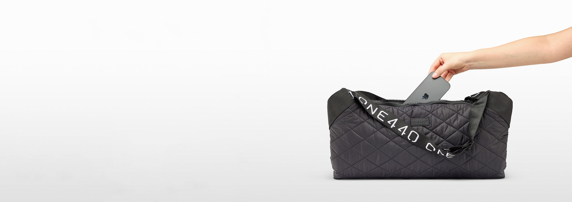 Person opening a black quilted one440 bag on a white background